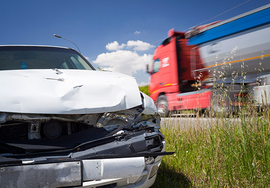 a car with a damaged front end and a red semi truck in the background